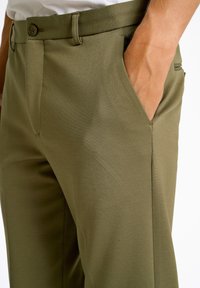 Olivgrüne Hose aus glattem Material, mit Knopfverschluss, Fronttaschen und einem maßgeschneiderten Schnitt mit klarer Silhouette.