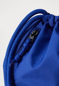 Sac à cordon en tissu bleu avec une surface texturée, matériel de fermeture éclair noir et cordons tressés, mettant en avant des éléments de design pratiques.