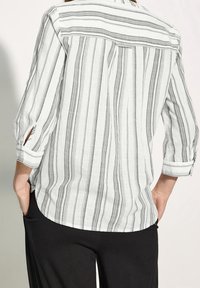 Chemise boutonnée en tissu léger avec des rayures verticales noires ; comporte des manches 3/4, des pattes de roulage et un détail de empiècement à l'arrière.