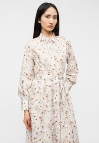 Φόρεμα με μακριά μανίκια από ελαφρύ ύφασμα με λουλουδάτο μοτίβο σε ροζ, πορτοκαλί και πράσινο. Διαθέτει γιακά και ζωνάκι στη μέση.