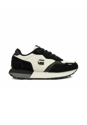 Zapatilla baja negra y blanca con cierre de cordones, paneles de ante negro y cuero blanco, y suela de goma con patrón de banda de rodadura.