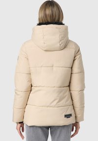 Padded beige jacket with a hood, featuring horizontal stitching, a black faux fur trim, and a brand tag on the lower back.