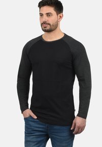 Black long-sleeve t-shirt with dark grey raglan sleeves, round neckline, and soft fabric. Jeans with a pocket are also visible.