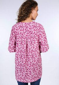 Fuchsia floral tunic with long sleeves, featuring small white flowers, a round neckline, and a back pleat detail. Soft fabric, relaxed fit.