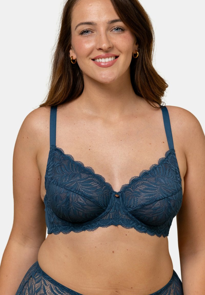 Soutien-gorge en dentelle bleu profond avec des motifs floraux, tissu semi-transparent, bords ondulés et bretelles ajustables avec un bouton décoratif central.
