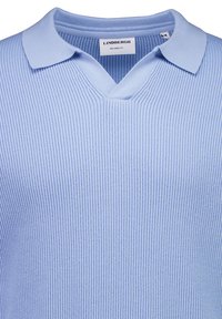 Lyseblå ribstrikket polo med afslappet pasform og blød krave, vist fra øvre bryst til kraveområde.