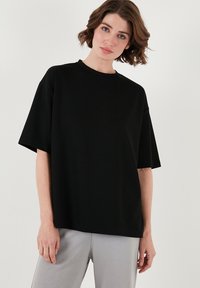 Melna oversized T-kreklā, kas izgatavota no gludas kokvilnas auduma. Iezīmēta ar apaļu dekoltē, īsām piedurknēm un brīvu piegriezumu. Nav redzamu rakstu vai akcentu.