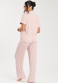 Set di pigiama rosa composto da una maglietta a maniche corte con colletto e bordi, abbinata a pantaloni lunghi e larghi. Texture morbida e a coste.