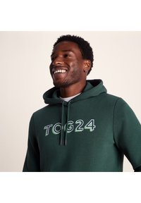 Green hoodie featuring a front logo "TOG24" in white and light green, adjustable drawstrings, and a soft cotton texture.