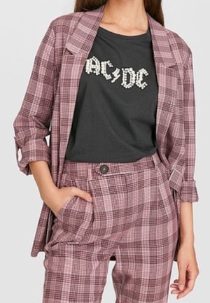 Vrouw draagt een roze en paarse geruite blazer en bijpassende broek met een zwart T-shirt met AC/DC-logo ingestopt.