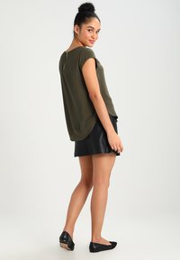 Olive green short-sleeve top with a curved hem and back zipper detail, paired with a black leather flared skirt and black flats.