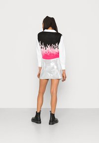 Colete preto com design de chamas rosa na bainha, usado sobre uma camisa branca e combinado com uma saia-minisilver e botas de tornozelo pretas.