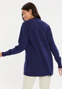Cardigan azul marino hecho de tejido de punto texturizado con un patrón de diamantes, que cuenta con mangas largas y puños y dobladillo acanalados.