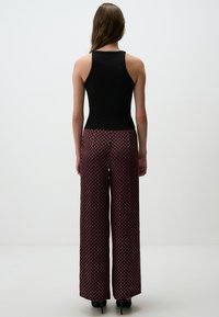 Zwart geribbelde tanktop gecombineerd met wijde broek met een geometrisch rood en zwart patroon, gladde stof en een relaxte fit.