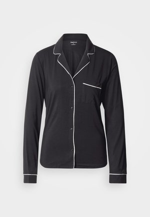 Svart pyjamasoverdel med lange ermer laget av mykt stoff, med hvite kantdetaljer langs kragen, knappestolpen og lommen. Klassisk knappeopp-design.