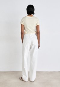 Camiseta de color beige claro con mangas cortas, combinada con jeans anchos blancos que tienen un bolsillo trasero y una cinturilla con marca.