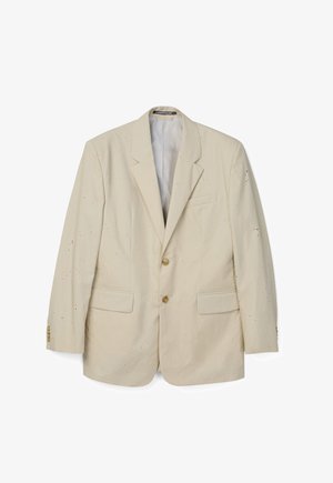 Blazer beige de un solo botón con dos botones, solapas con muesca, bolsillos con solapa y pequeños agujeros dispersos por toda la tela.