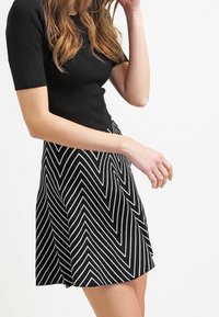 Zwarte, aansluitende top gecombineerd met een uitlopende rok met witte chevronstrepen, die een gladde textuur en een knielange stijl laat zien.