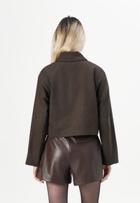 Brun kort jacka med en strukturerad tyg, med en klädd krage och långa ärmar, parat med bruna lädershorts.
