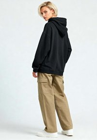 Felpa nera con cappuccio abbinata a pantaloni cargo beige larghi. Sneakers bianche e tasche laterali sui pantaloni. Design semplice, informale e senza decorazioni.