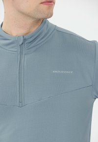 Lyseblå halv-zip sportsbluse med et struktureret mønster, høj krave og subtilt logo. Har struktureret stof med en tætsiddende design.