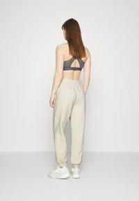 Sujetador deportivo en gris oscuro con un diseño de espalda cortada, combinado con pantalones de chándal beige ajustados y zapatillas ligeras de color verde.
