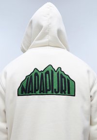 Felpa bianca con grafica di una montagna verde e testo nero "NAPAPIJRI" sul retro. Presenta un cappuccio con cordoncino e una texture morbida.