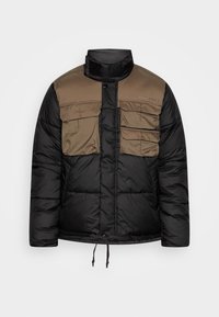 Giacca trapuntata con una parte inferiore nera e una parte superiore color beige. Presenta due tasche sul petto, chiusura con bottoni a pressione e orlo regolabile con cordoncino.
