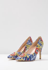 Chaussures à talons aiguilles à bout pointu avec un motif floral bleu et jaune sur le tissu, dotées d'une semelle intérieure nude et d'un talon fin.