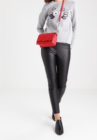 Felpa grigia con dettagli grafici colorati, leggings in pelle nera e una borsa a tracolla rossa con manico a catena. Mocassini neri.