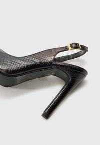 Scarpa nera con tacco alto e slingback, con una finitura testurizzata a motivo rettile. Presenta un dettaglio con fibbia sulla cinghia, punta affusolata e tacco lucido.