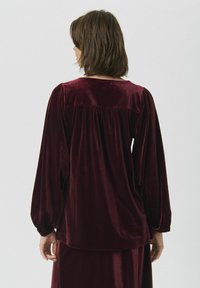 Bordeaux-rotes Samt-Oberteil mit puffierten Ärmeln, einem runden Ausschnitt und Raffung am Rücken, mit einer glatten, weichen Textur.