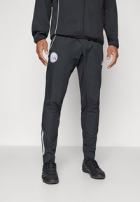 Sorte sportbukser med elastisk talje, med hvide sidestriber og et rundt logo på venstre lår. Lavet af letvægtsstof.