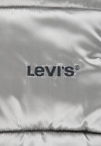 Srebrna tkanina s mekanom teksturom, sa izvezenim crnim logotipom "Levi's". Vidljive šavove s detaljima šivanja.