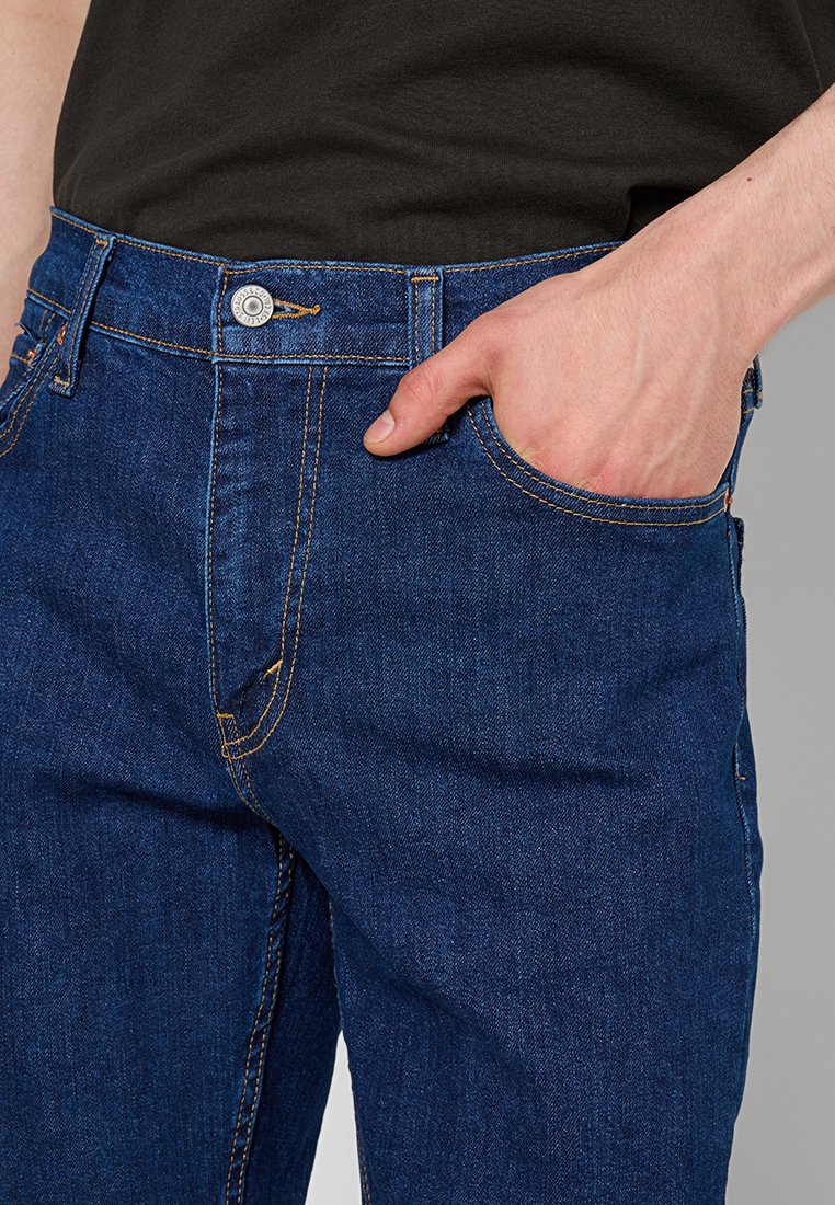 Denim jeans featuring a dark blue color, classic five-pocket design, visible stitching in orange, and a metal button at the waistband.