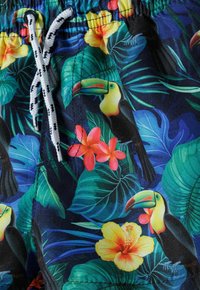 Bañador con un vibrante estampado tropical que presenta tucanes, flores de hibisco y hojas verdes sobre un fondo azul oscuro. Cintura ajustable con cordón.
