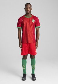 Marockanskt landslagsfotbollskit med en röd tröja med gröna accenter och stjärnmönster, röda shorts, gröna strumpor och svarta skor.