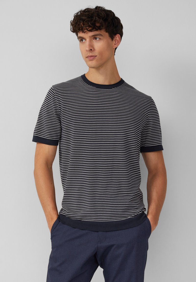 Pasiasta koszulka z krótkim rękawem w kolorze granatowym i białym, z okrągłym dekoltem i jednolitym granatowym wykończeniem rękawów oraz dołu. Miękka tkanina, luźny krój.