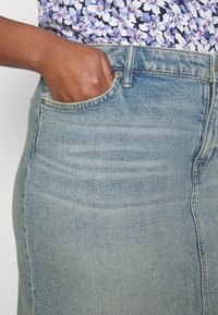 Ljust blå denimkjol med rakt snitt, med en ficka framtill och synliga söm detaljer. Tyget ser ut att vara något slitet.