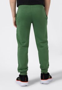 Groene joggingsbroek met een gladde textuur, met enkelboorden en zijzakken, gecombineerd met zwarte sneakers met een oranje accent.