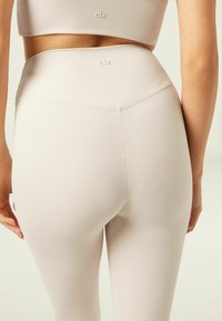 Leggings beige a vita alta realizzati in materiale elasticizzato, caratterizzati da un marchio discreto e da una finitura liscia e testurizzata con una silhouette aderente.