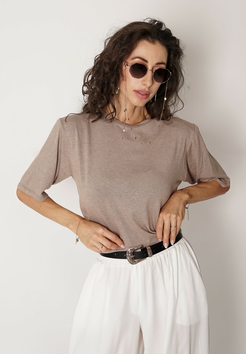 Beżowa bluzka z krótkim rękawem noszona z czarnym paskiem z srebrną klamrą, w zestawie z białymi spodniami typu wide-leg. Dodatki to kolczyki łańcuszkowe i okulary przeciwsłoneczne.