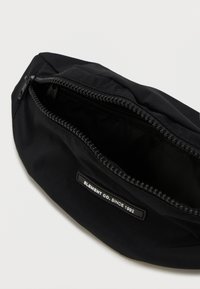 Custodia nera con zip, dal design liscio, che presenta una piccola etichetta "Element Co. Since 1992" e un interno della zip di colore nero a contrasto.