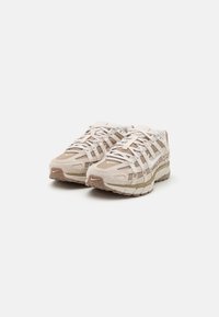 Beige sportskor i mesh och mocka, med en texturerad sula och flera snörningsöppningar. Rundade tår och vadderad design.