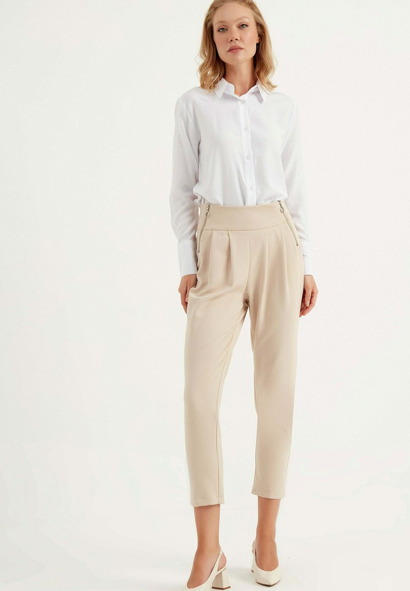 Witte overhemd met knopen in combinatie met beige geplooide broeken met zijritsen, een zachte textuur en een cropped lengte. Klassieke hakken maken de look compleet.