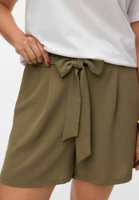 Olivgröna shorts i ett texturerat material, med en framknuten rosett vid midjan och sidofickor. Bärs tillsammans med en vit topp.