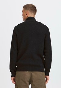 Schwarzer Strickpullover mit strukturiertem Waffelmuster, hohem Kragen und gerippten Bündchen. Verfügt über eine entspannte Passform und eine einfarbige dunkle Farbe.