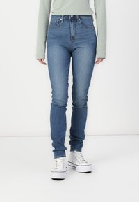 Traperice s visokom strukom u plavoj boji, uskog kroja, s minimalnim šavovima, pet džepnim dizajnom i blagim izblijedjenjem duž nogavica.