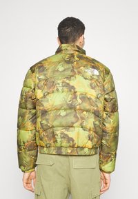 Zelená a hnědá maskáčová prošívaná bunda s elastickým lemem. Na horní části zad má bílé logo.