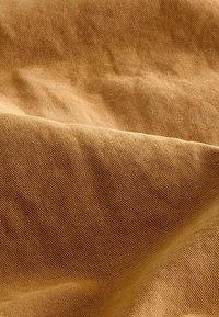 Meleg mustársárga pamutfabric, textúrált szövettel, amelyben látható szálak és lágy redők találhatók, kellemes, barátságos megjelenést kölcsönözve.